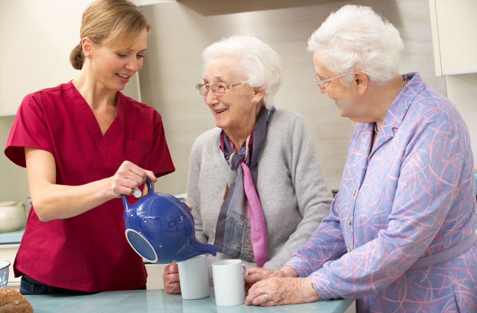 An assisted living staff pouring tea for a pair of older adult women.