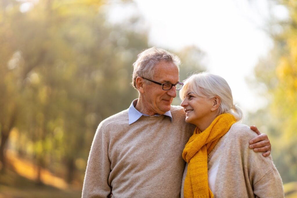 Senior man and woman embracing outside while smiling.