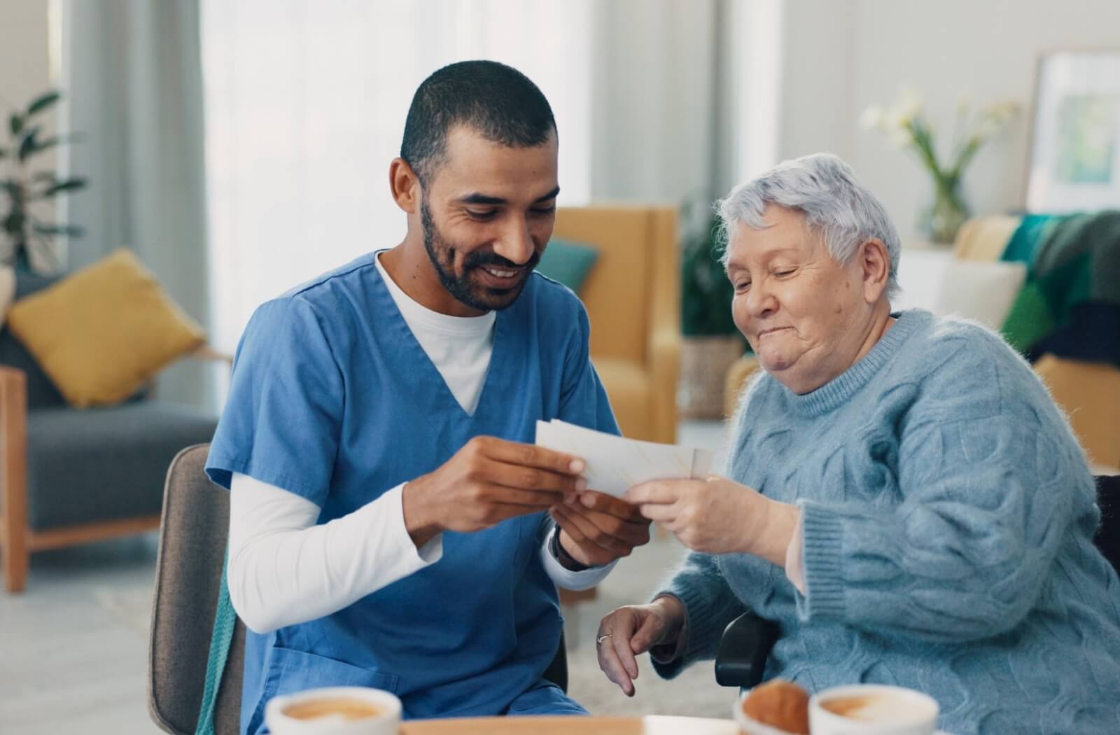 A smiling staff member in memory care and an older adult sitting together, looking through photos.