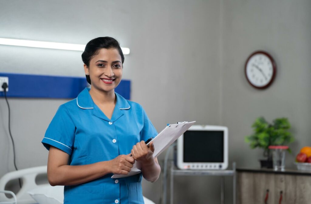 A smiling nurse wearing blue scrubs and standing with a clipboard in her hands in a skilled nursing community.