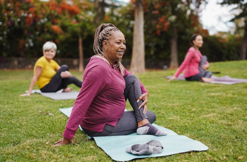 Three seniors stretch out on yoga mats on an outdoor field during a yoga class hosted at an assisted living community