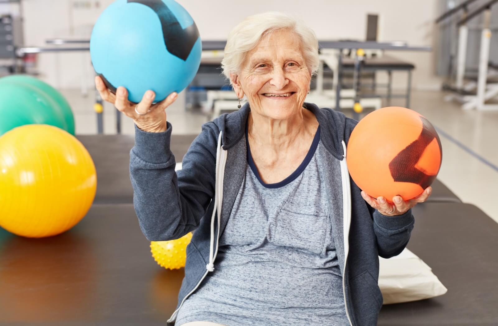 A happy, mature adult holding 2 medicine balls used in occupational therapy