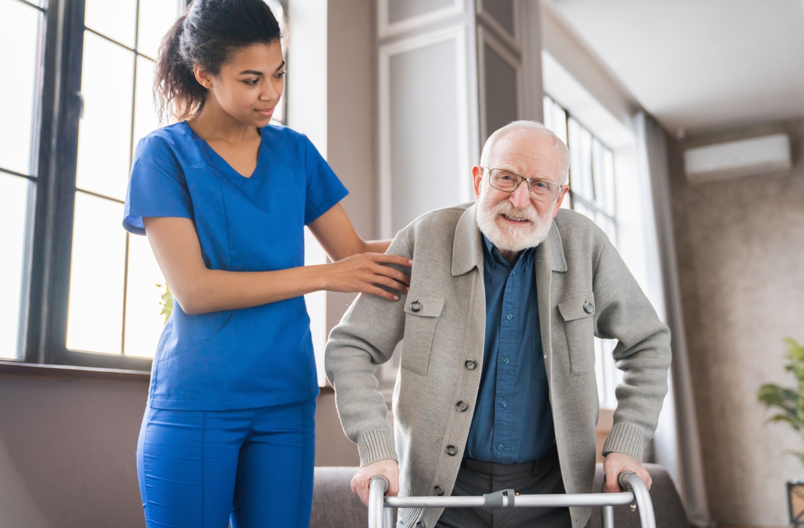 A therapist assists an older adult move around using a walker.