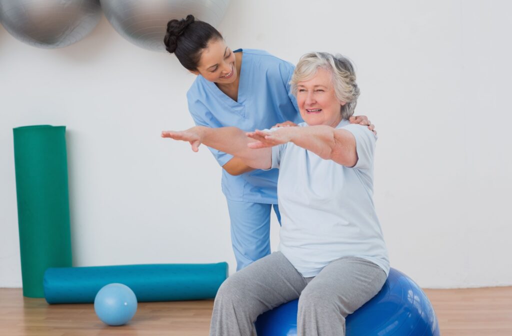 An occupational therapist shows a senior with a yoga ball some exercises to prevent falls.