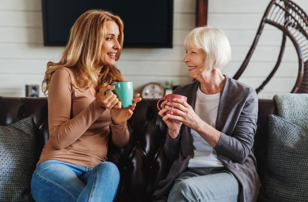 Younger woman and older woman talking on a couch while drinking out of mugs.