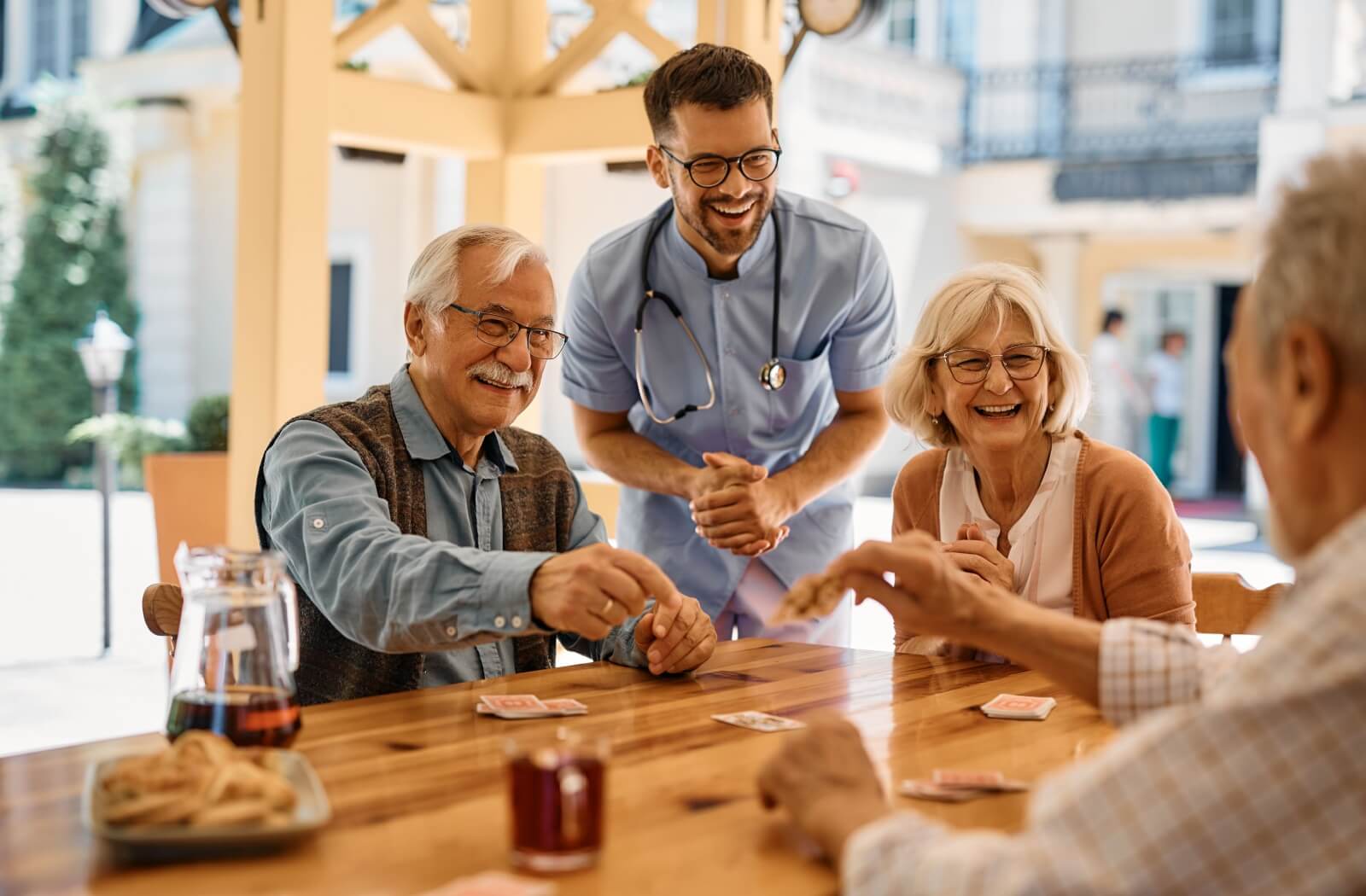 A group of assisted living residents cheerfully playing a game of cards while a staff member happily observes.