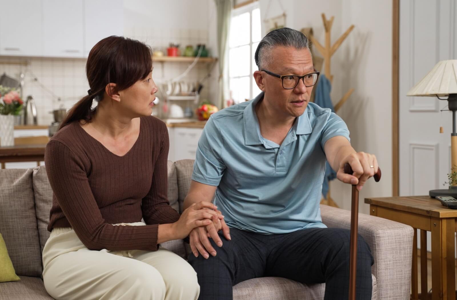 While sitting on the couch, an adult expresses concern to their older parent about their memory, holding their hand