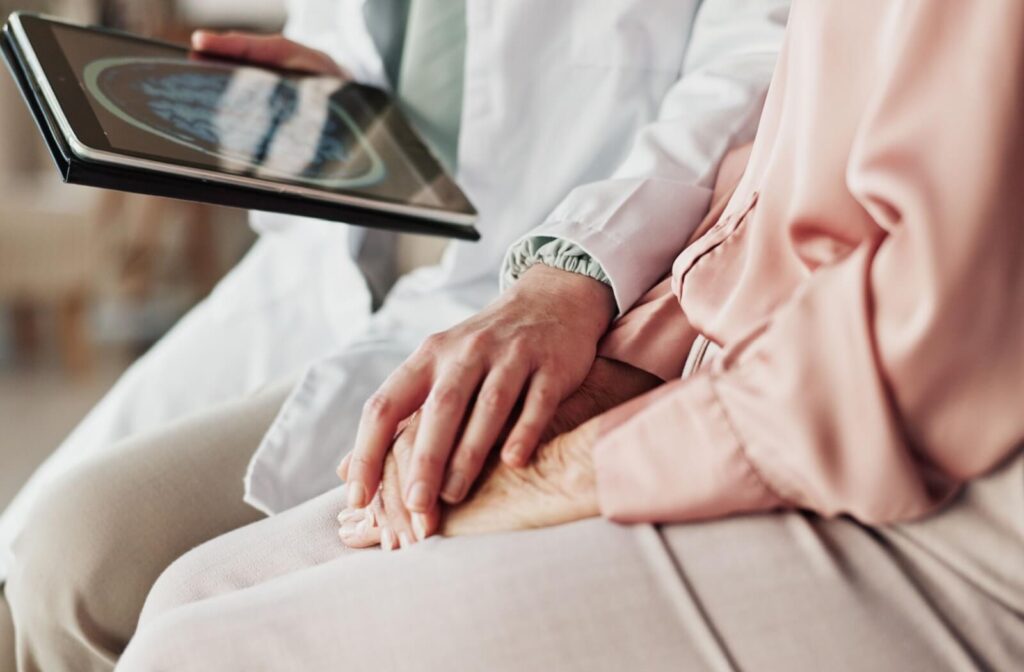 A doctor provides emotional support in a gentle hand touch while discussing a dementia diagnosis with a senior