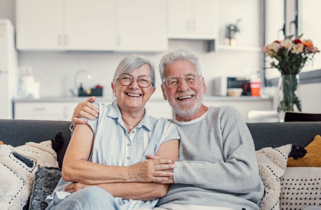 senior couple sitting in their all-inclusive senior living apartment holding each other and smiling