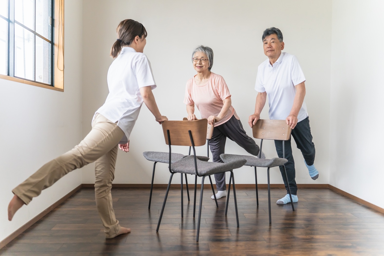 Older man and woman doing chair exercises and rehabilitation at a nursing facility, with physical therapist and caregiver present.