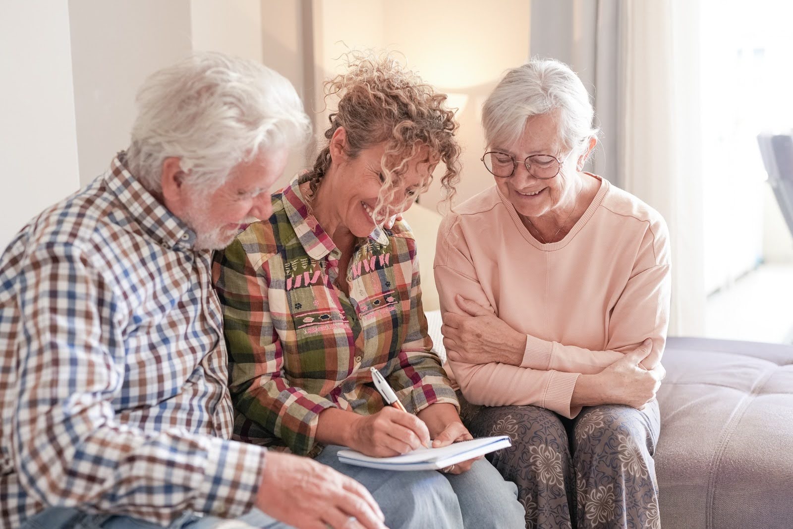 An older couple and their adult child sit together in a bright living room while discussing questions from a notepad.