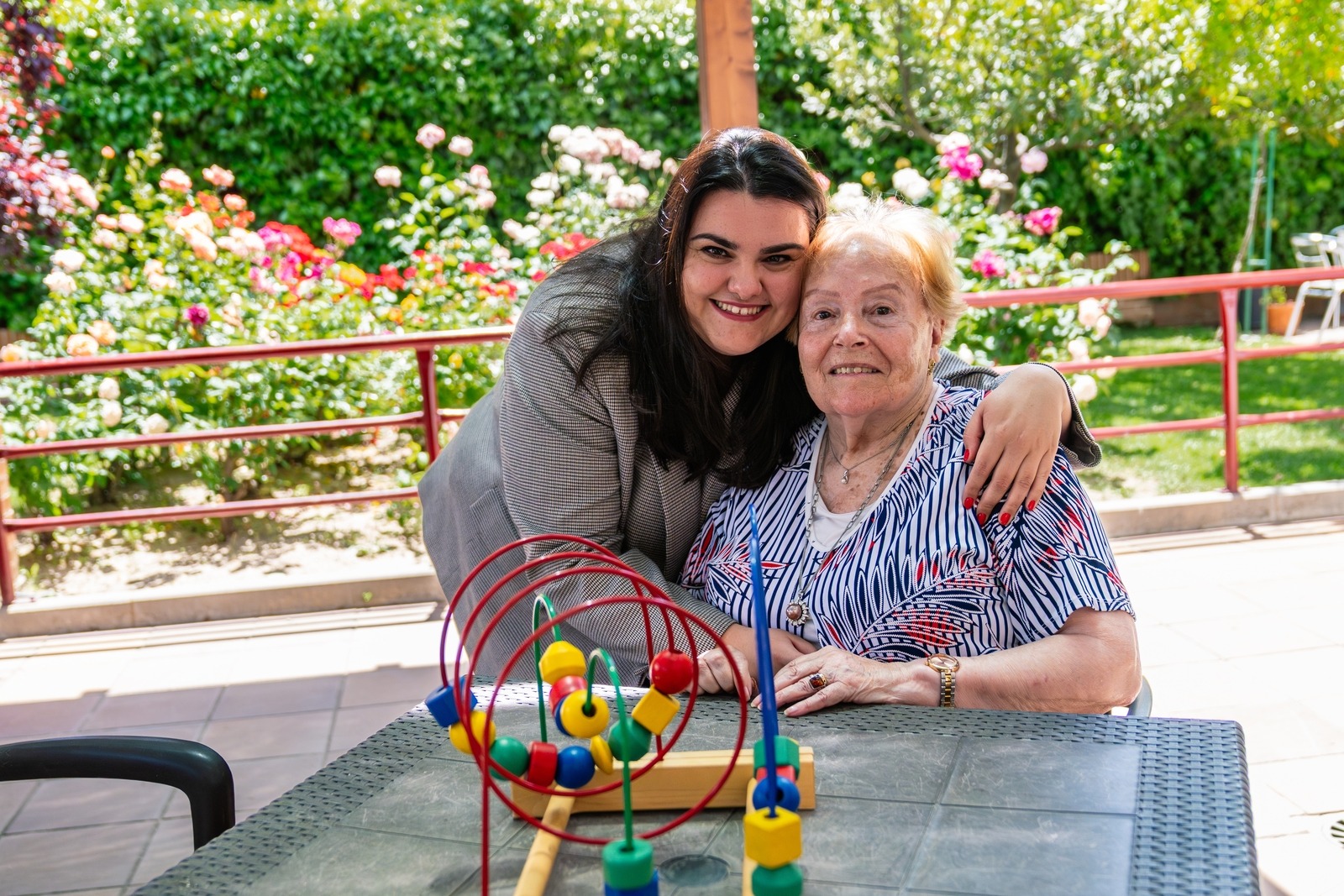 A caregiver and an older woman use a bead maze together in a garden.